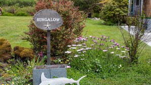 Un letrero con la palabra 'BUNGALOW' y un símbolo de estrella de mar, rodeado por un jardín con diversas plantas y flores.