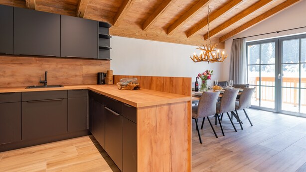 Una cocina moderna con vigas de madera, una isla de madera, armarios oscuros y un comedor con vistas.