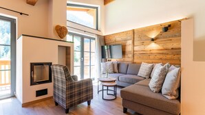 Una sala de estar moderna con chimenea, un sofá, un sillón escocés y un televisor montado en la pared.