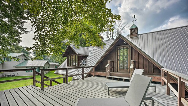 Um deck de madeira com mesa e cadeiras, com vista para uma área residencial com casas e uma grande árvore.