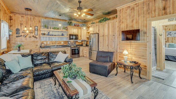 A spacious living area with a leather sofa, a dining table, and a kitchen with wooden cabinets and modern appliances. - 'Grace Place' Clark House on Farm: Shared Hot Tub! (Clark)