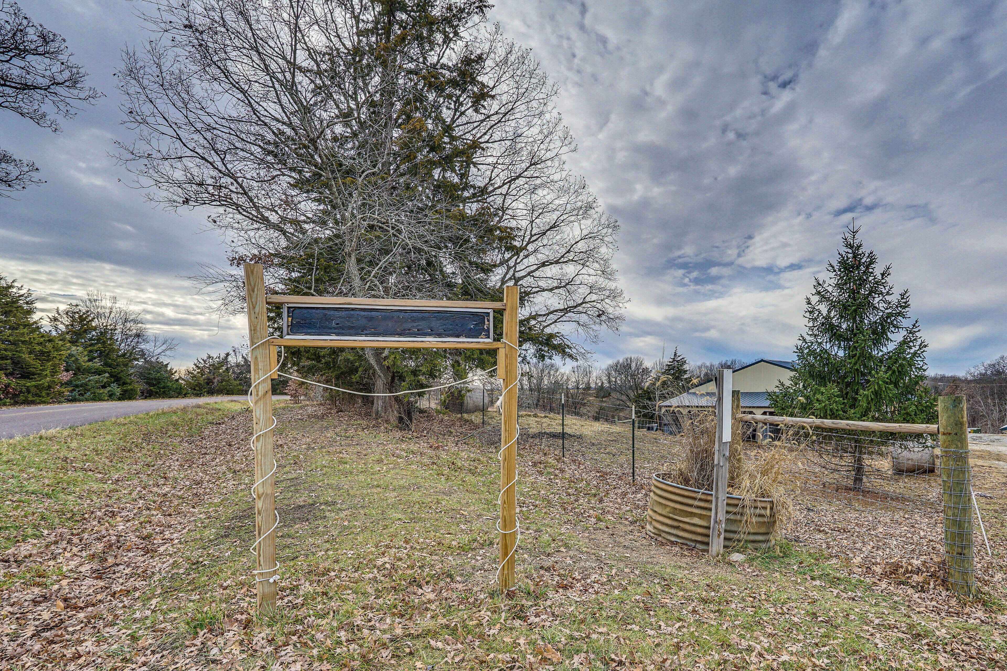 A wooden signpost in a grassy area with a fence and trees in the background.