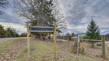 A wooden signpost in a grassy area with a fence and trees in the background.