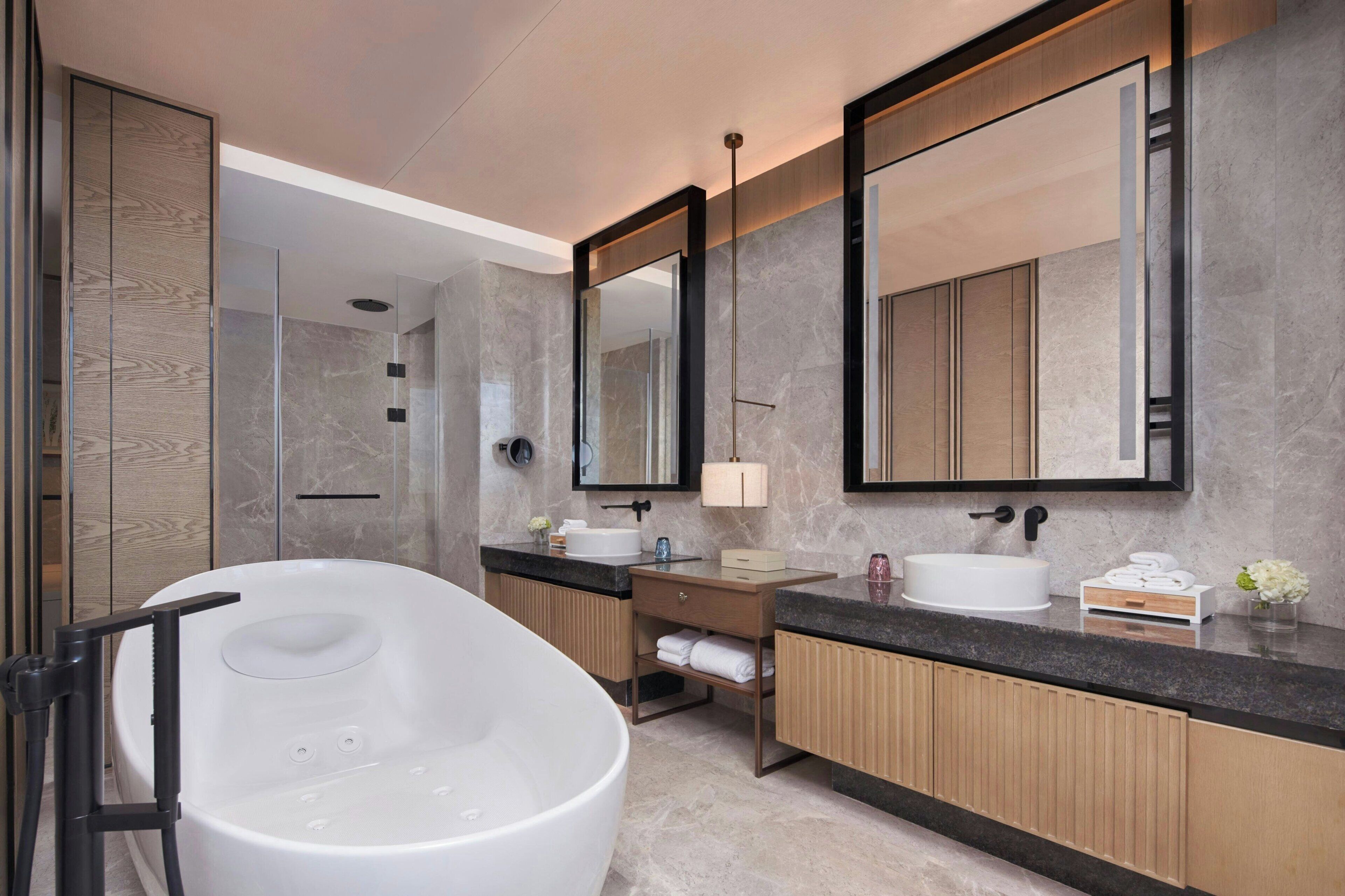 Un baño moderno con una bañera independiente, un espejo grande y un lavamanos con lavabo y toallero.