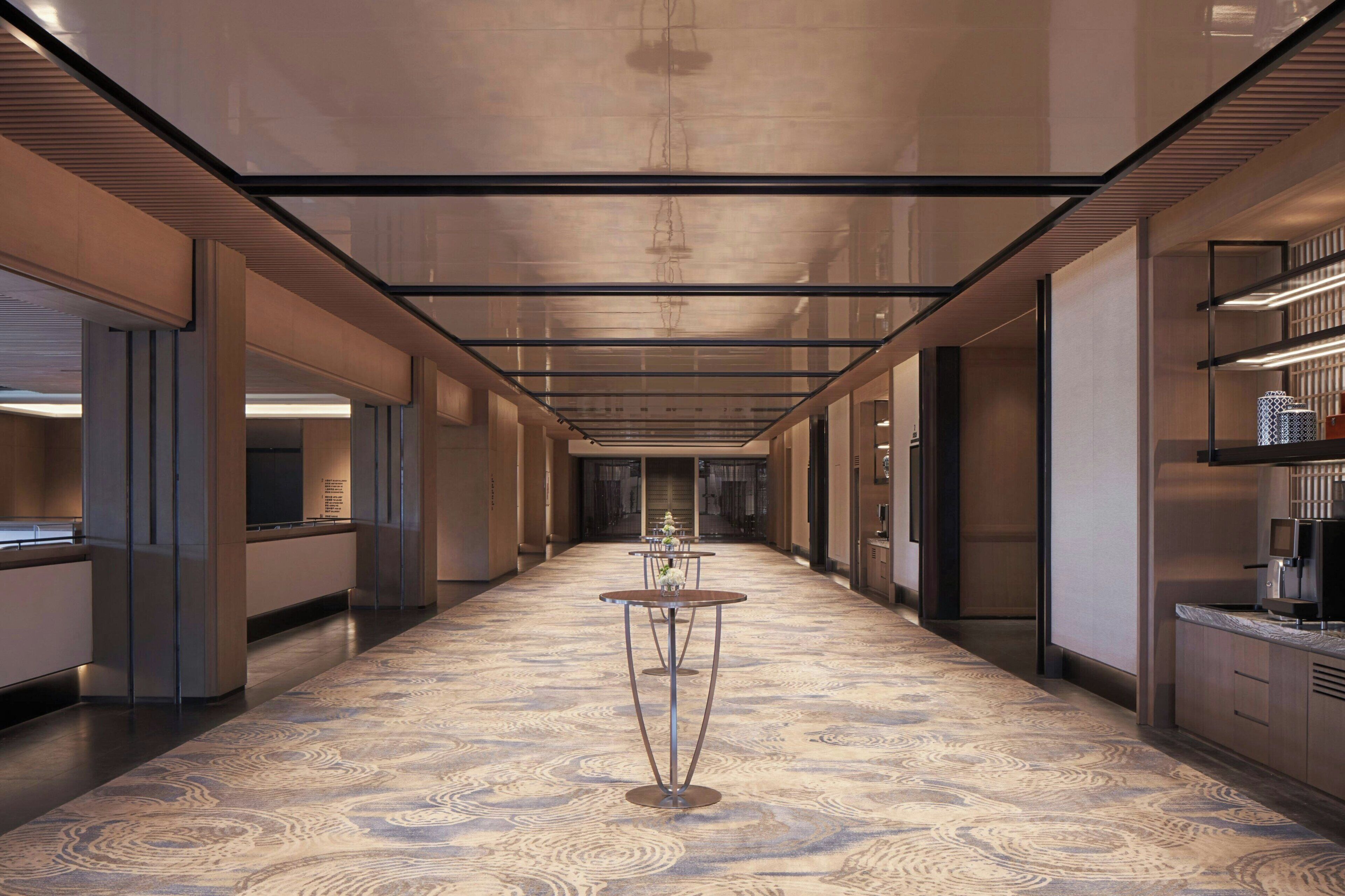 A long hallway with a patterned floor, tables with vases, and modern lighting.