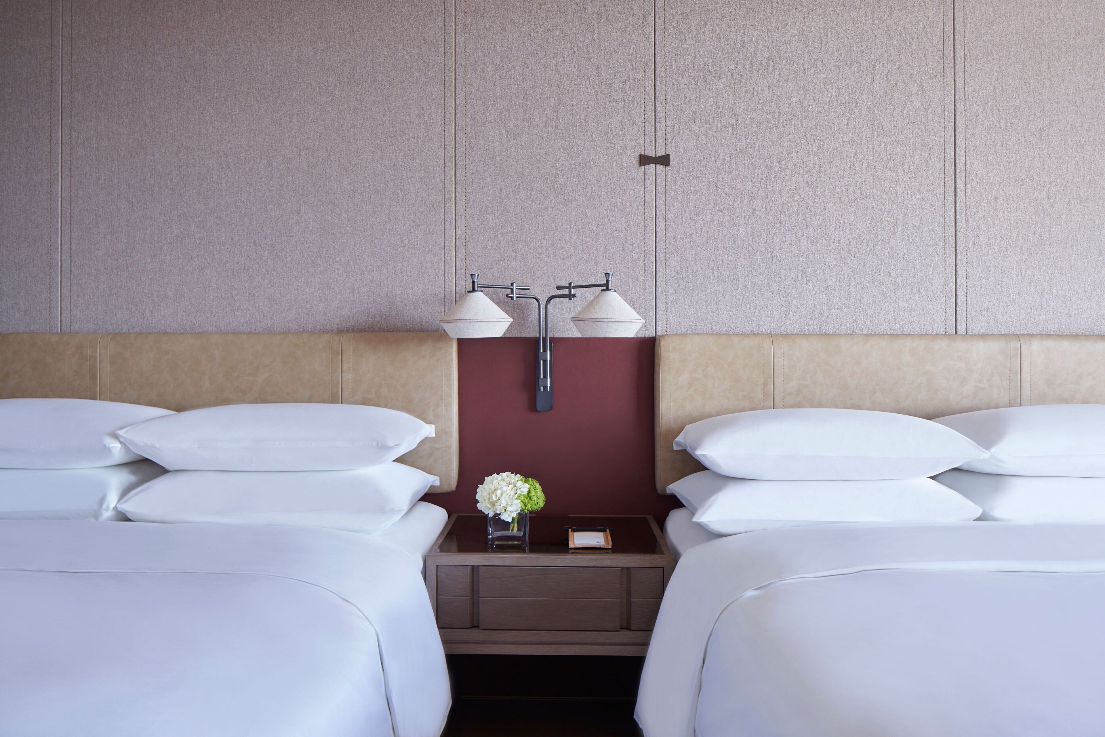 A hotel room with two beds, a nightstand with two lamps, and a vase with flowers.