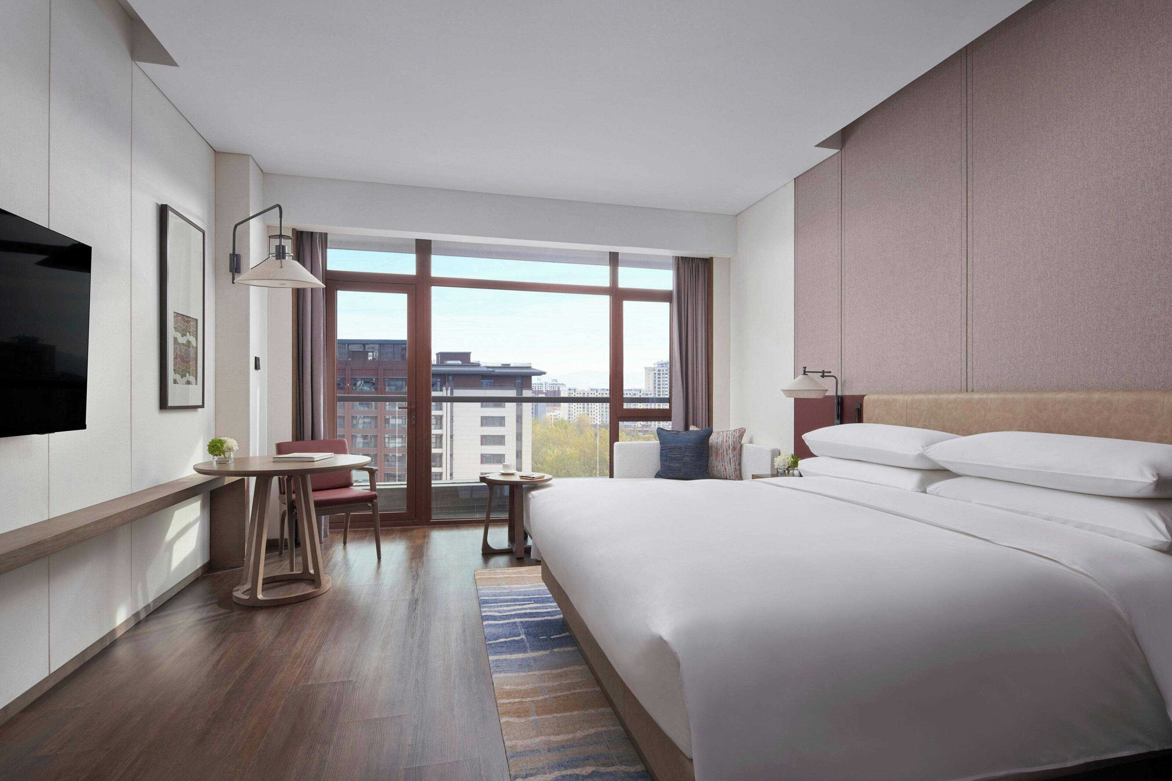 A modern hotel room with a large bed, a desk, a chair, and a television.