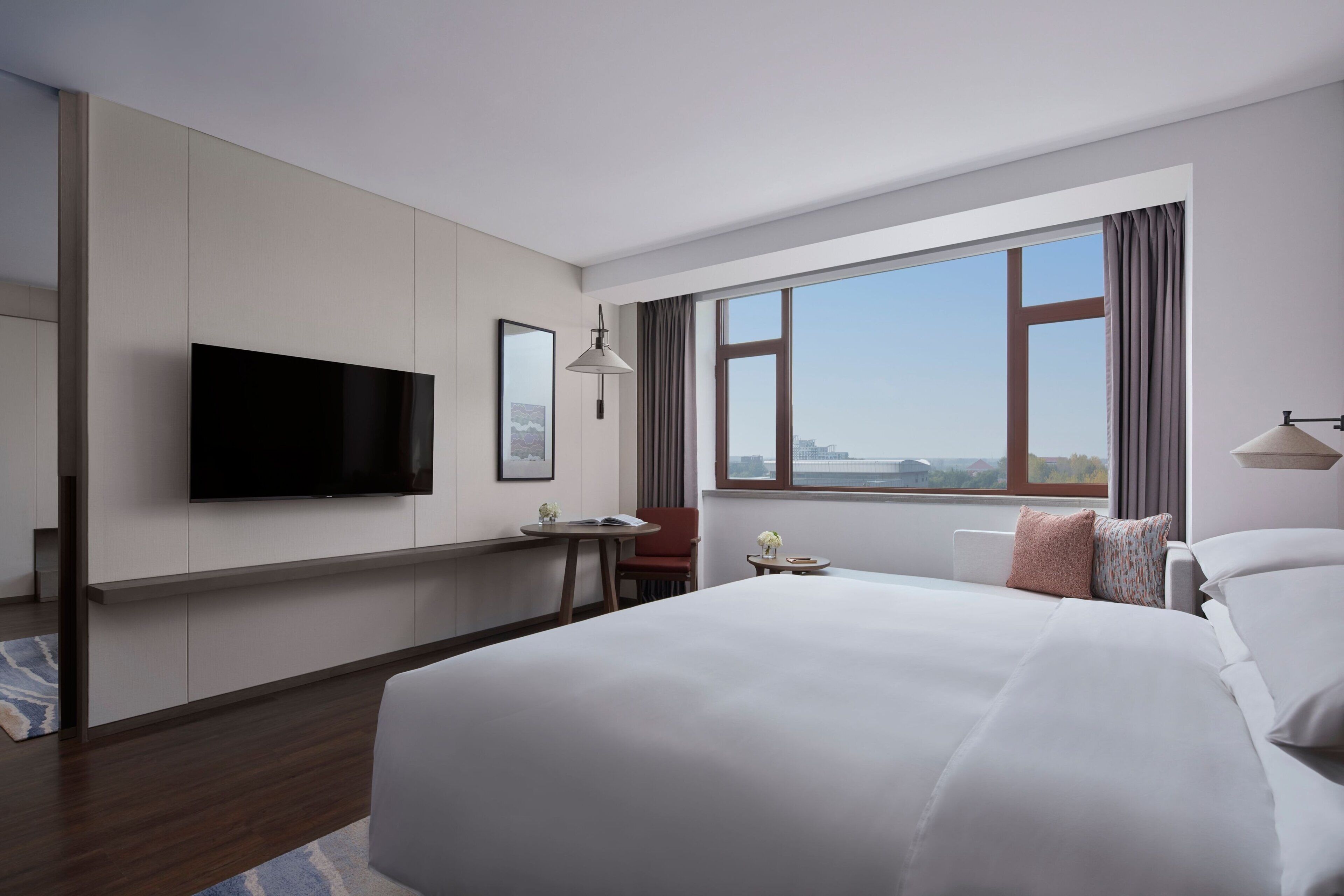 Habitación de hotel con una cama grande, un televisor de pantalla plana montado en la pared, un escritorio con una silla y una ventana con vistas a la ciudad.