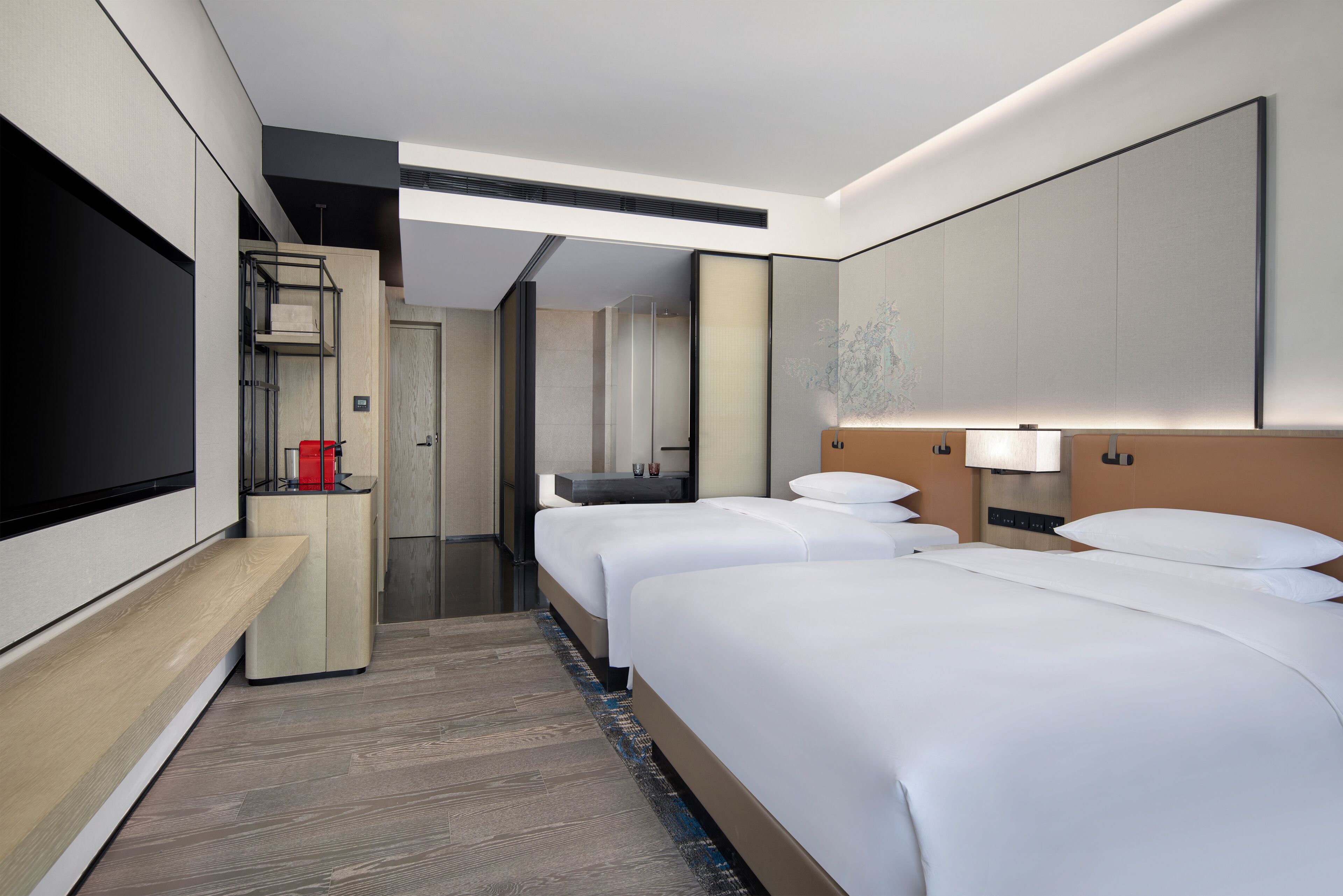A hotel room with a large flat-screen TV, two beds, a desk, and a bathroom.