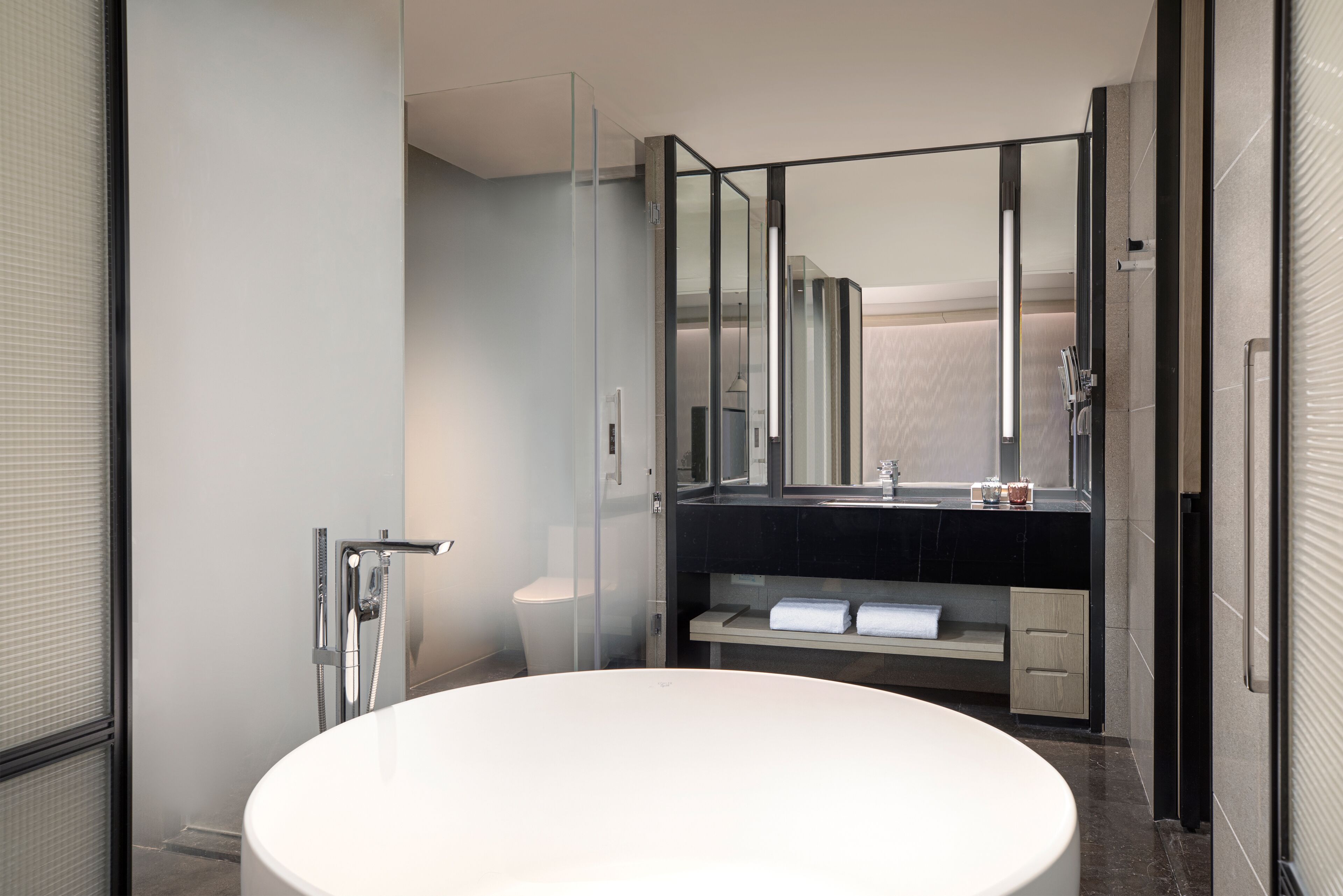 Une salle de bain moderne avec un grand lavabo ovale, une douche en verre et un comptoir noir agrémenté d’un miroir.