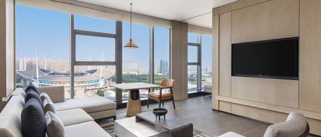 A modern living room with a large TV, comfortable seating, a dining area, and a view of a cityscape.