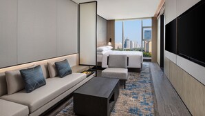 Una habitación de hotel moderna con sofá, una mesita, cama y televisor grande.