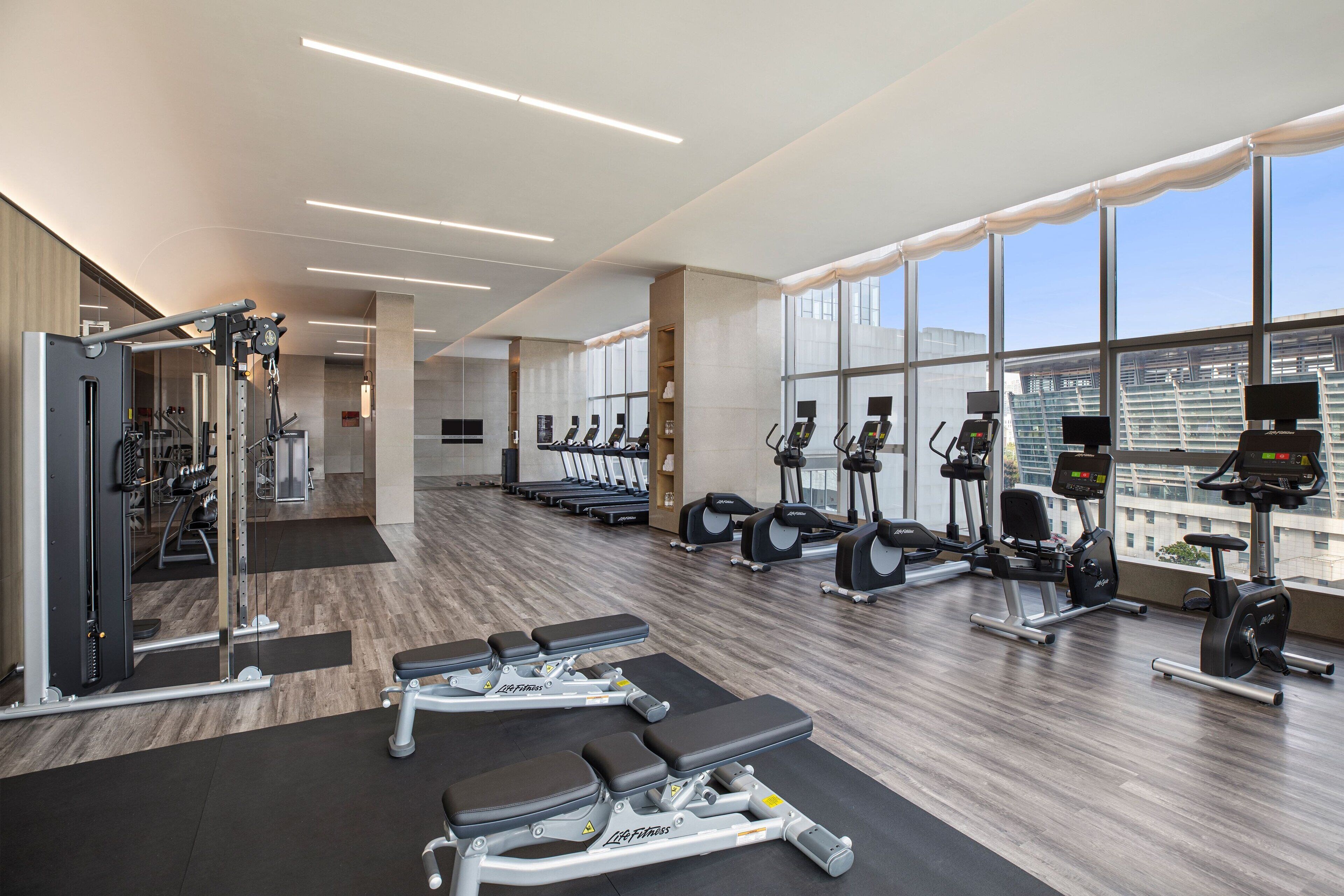 Un gimnasio moderno con máquinas cardiovasculares, pesas y bancos.