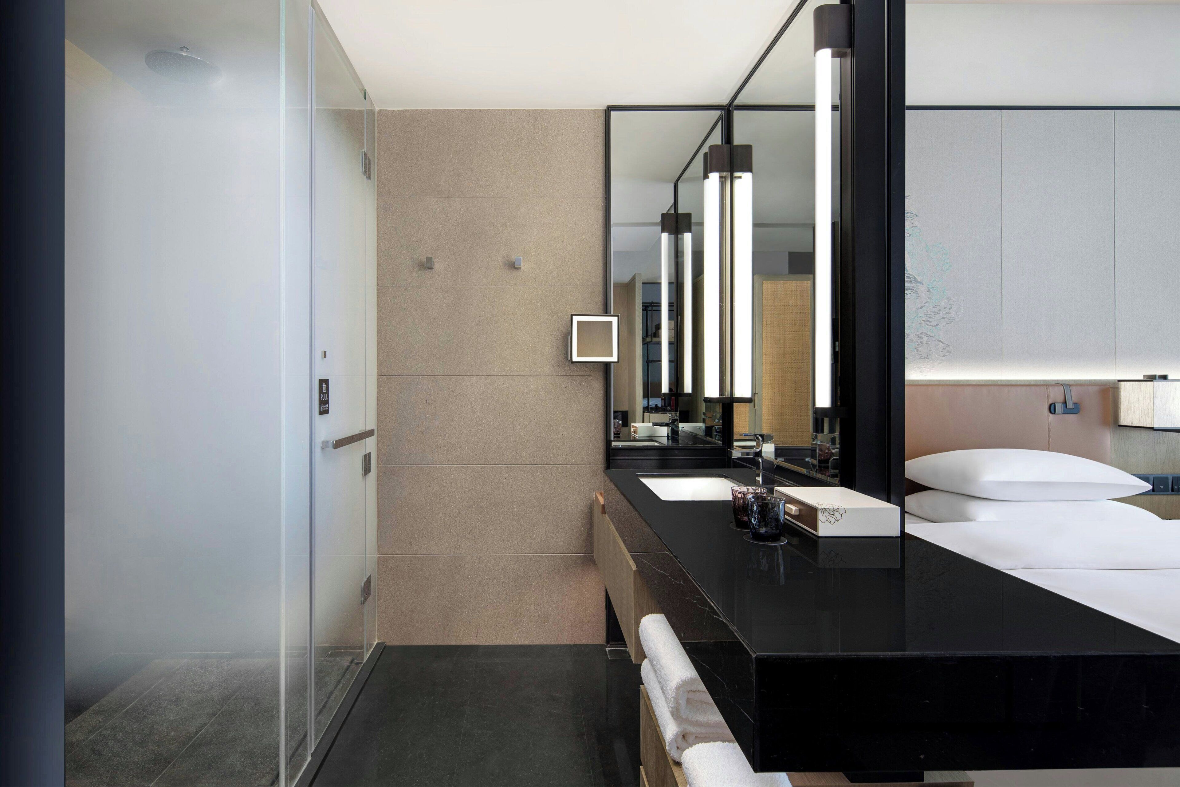 Un baño moderno con cabina de ducha de vidrio, un lavabo de mármol negro y un espejo grande que refleja la habitación.
