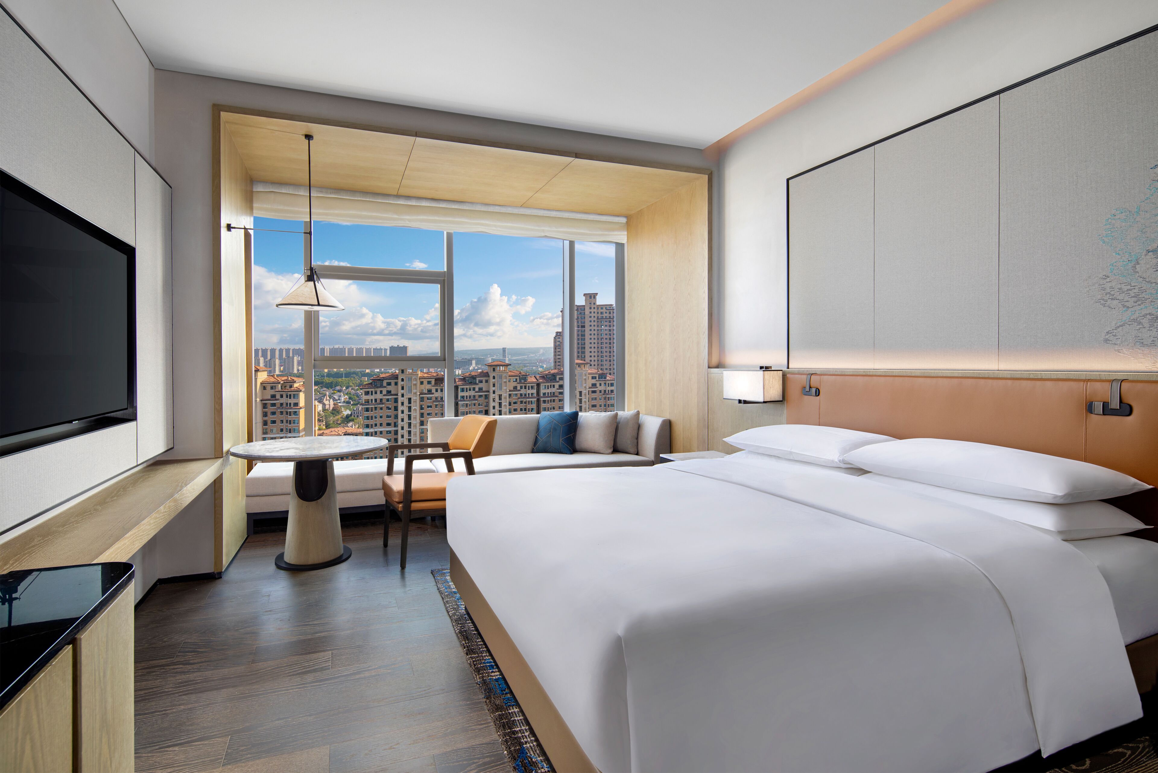A hotel room with a large bed, a TV, a seating area with a table, and a view of the cityscape.
