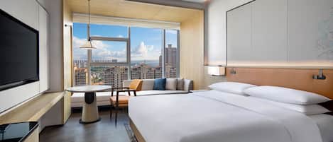 A hotel room with a large bed, a TV, a seating area with a table, and a view of the cityscape.