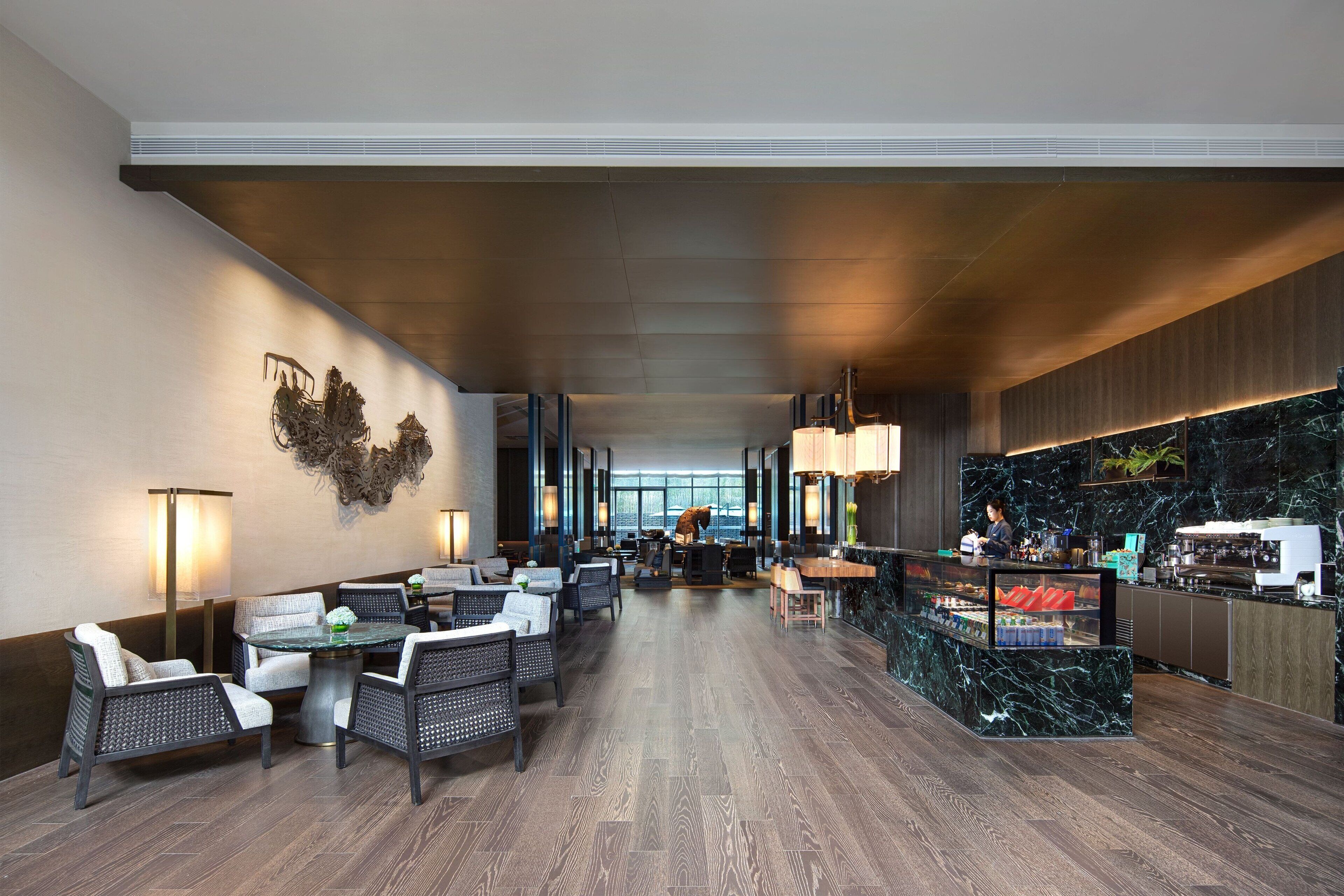 A modern hotel lobby with a central seating area, a bar, and a view of the city through large windows.