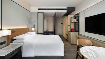 Una habitación de hotel moderna con una cama grande, un escritorio, una silla, un televisor y un minibar.