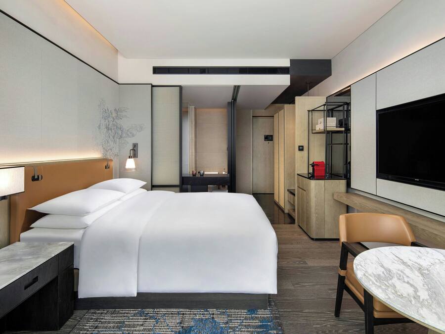 Una habitación de hotel moderna con una cama grande, un escritorio, una silla, un televisor y un minibar.