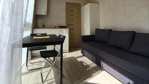 Un espacio habitable moderno y abierto con techo de madera, una zona de comedor con mesa y sillas, un sofá de color oscuro y una cocina con armarios y una puerta.