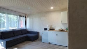 Una sala de estar moderna con un sofá modular, una kitchenette compacta y un techo de madera.