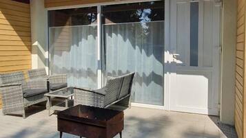 Un patio exterior con mobiliario de mimbre, una mesa y un cerramiento de vidrio corredizo que da a un acceso cubierto.