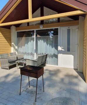 An outdoor patio area with wicker furniture, a table, and a sliding glass door leading to a covered entrance.