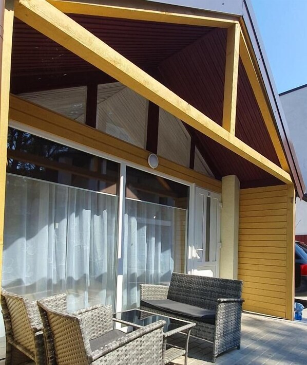 A covered outdoor seating area with wicker furniture and a glass table.