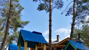 Un parque infantil con estructuras para escalar y toboganes, rodeado de árboles y un edificio al fondo.