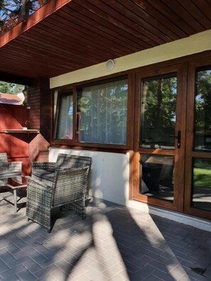 An outdoor patio area with wicker furniture, large windows, and a brick wall.