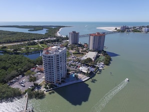 Vista aérea de uma área costeira com dois edifícios altos, uma marina e uma praia.