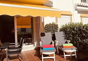 Une terrasse extérieure avec deux chaises longues blanches, un auvent jaune et un sol carrelé.