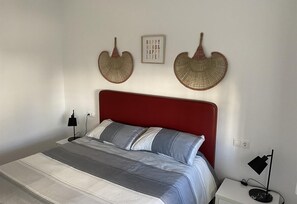 Une chambre à coucher avec une tête de lit rouge, un lit avec une literie à rayures, deux objets décoratifs fixés au mur et une table de chevet avec une lampe.