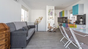 Un espacio de estar moderno con un sofá gris, cómoda de madera y un área de comedor con mesa y sillas de vidrio.