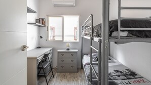 Un dormitorio con literas, un escritorio, una silla, un aparador y una ventana.