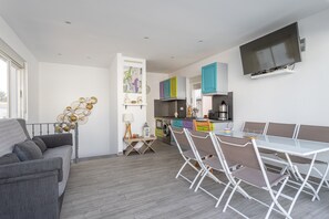 Ein zeitgemäßer Wohnraum mit Sofa, Esstisch, Stühlen, Küchenzeile und einem an der Wand befestigten Fernseher.