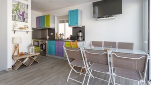 Una cocina moderna con armarios de colores, un comedor con mesa y sillas, una lavadora y un televisor instalado en la pared.