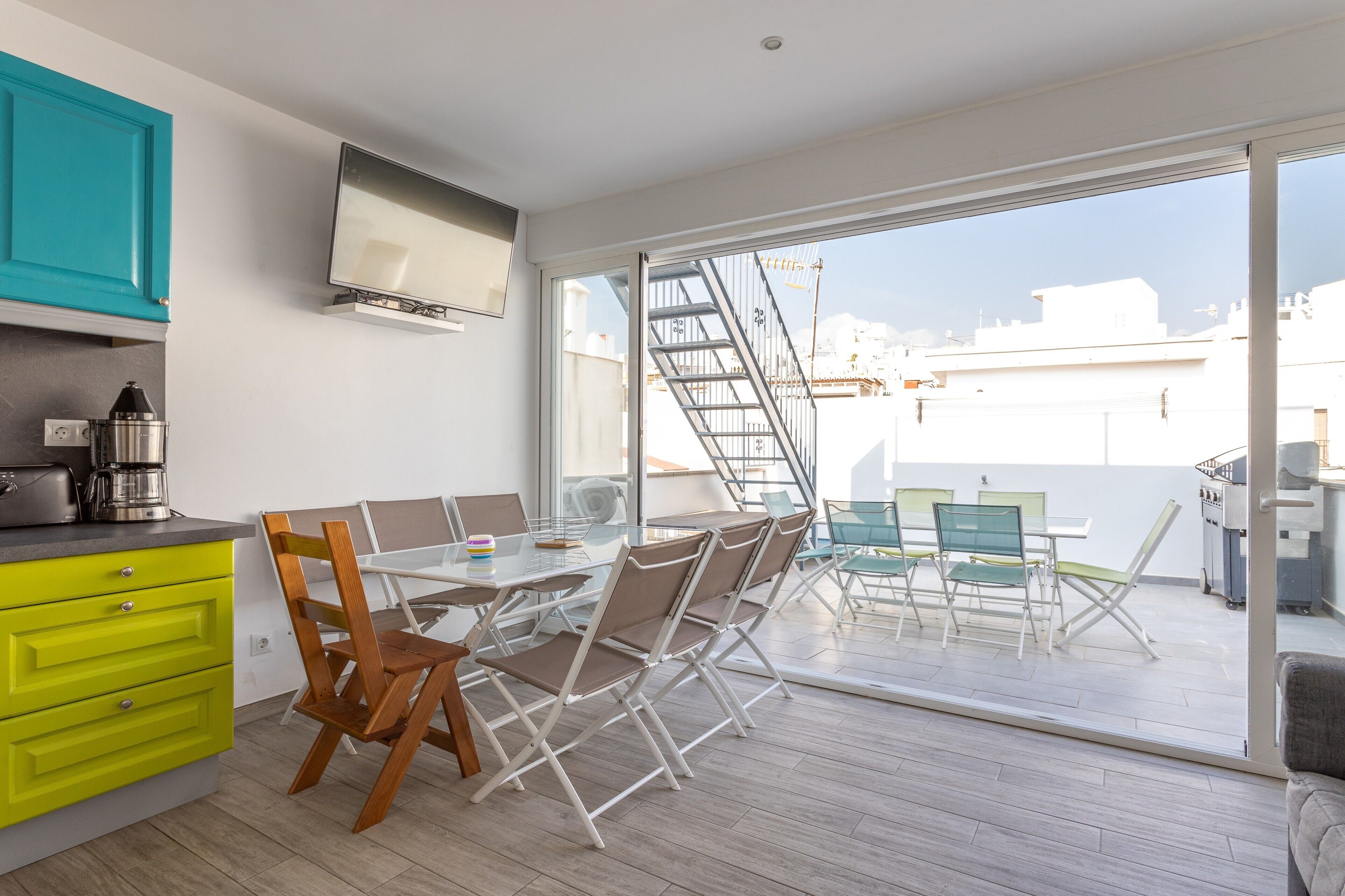 Een moderne keuken met een eethoek, een tv boven de aanrecht en een schuifdeur naar een terras.