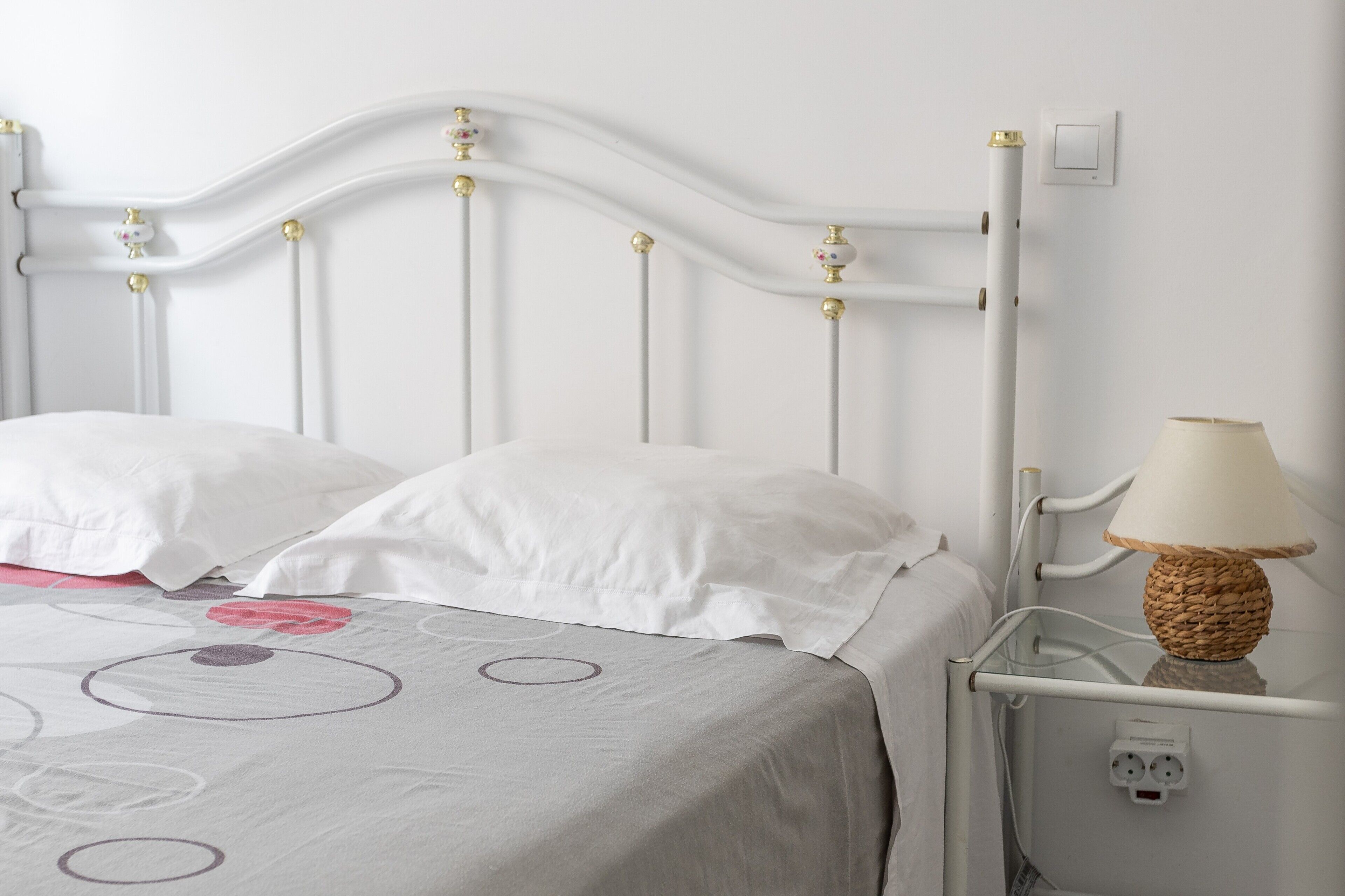 Een bed met een wit hoofdeinde, een bedlampje en een stopcontact aan de muur.