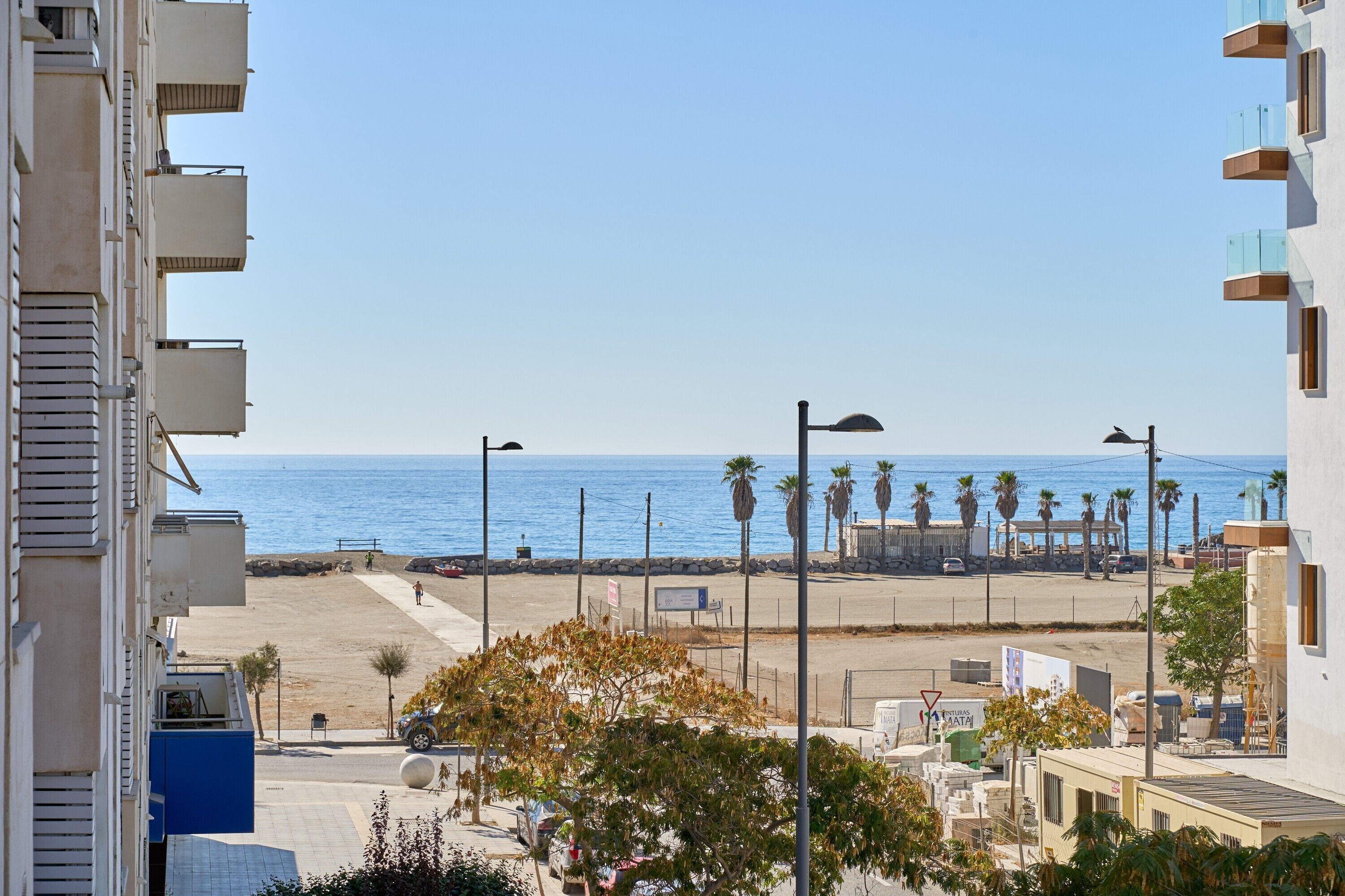A coastal view with a beach, palm trees, and a clear sky.