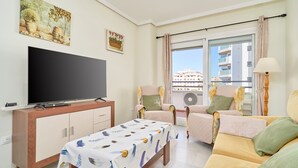 Una sala de estar con televisor, sofá, sillas, una mesa y un ventanal con vistas.