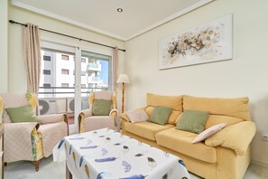 A living room with a sofa, chairs, a table, a lamp, and a window with curtains.