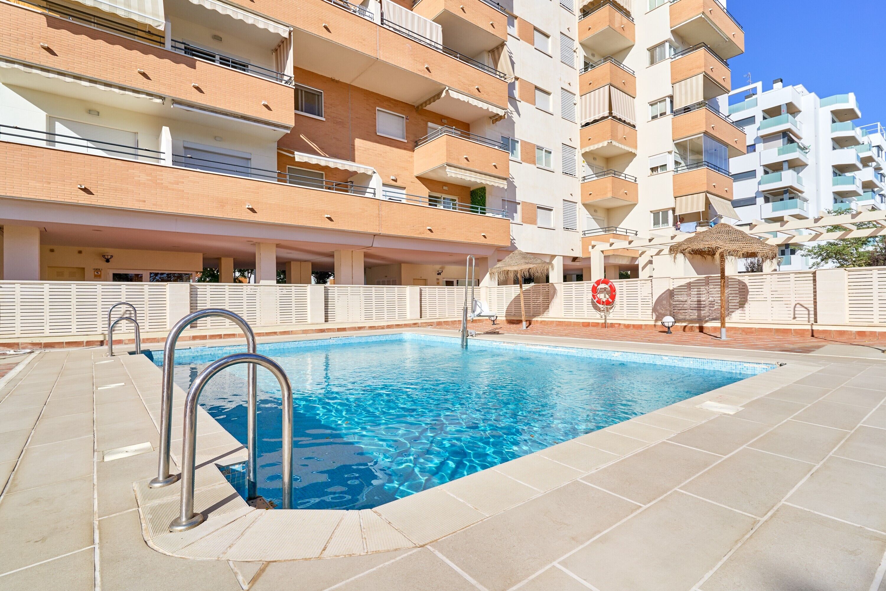 A swimming pool with metal railings, adjacent to a multi-story residential building with balconies.