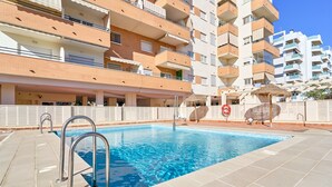 Una piscina con barandales de metal, junto a un edificio residencial de varios pisos con balcones.