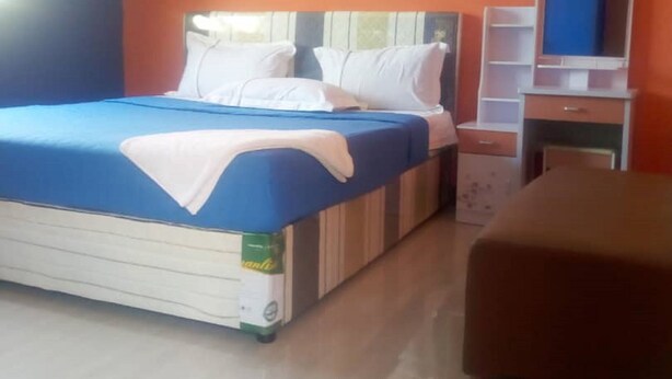 A bedroom with a bed, a nightstand, a dresser, and a mirror. - Muroy Executive Lodge (Kitwe)