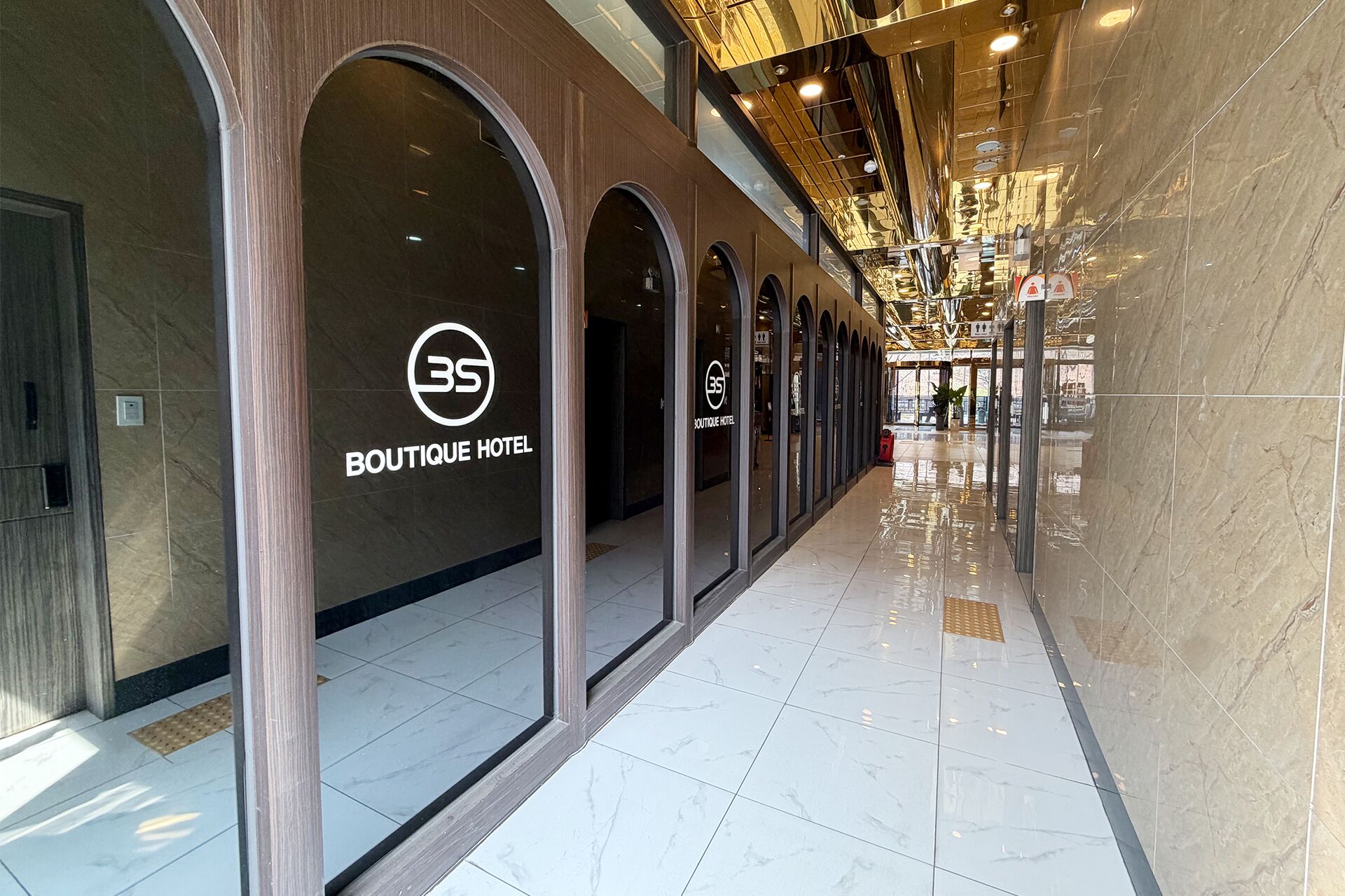Ein Flur mit einem Schild für ein Boutique Hotel, einer spiegelnden Decke und einem gefliesten Boden.