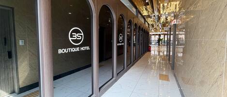 A corridor with a Boutique Hotel sign, reflective ceiling, and a tiled floor.