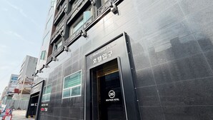Um edifício moderno com uma placa indicando um Hotel Boutique, grandes janelas e porta de entrada de metal.