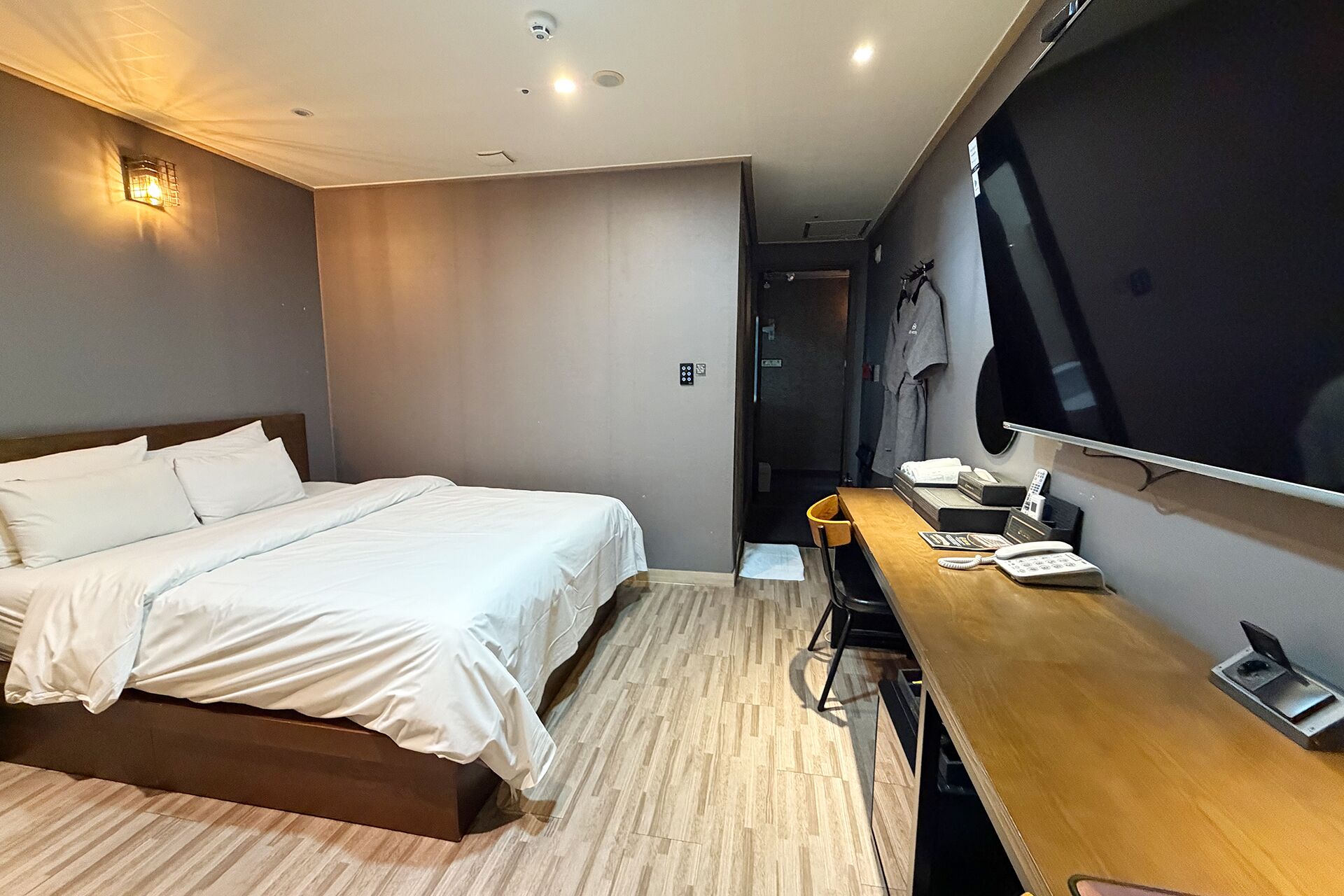 Una habitación de hotel moderna con cama, escritorio, televisor de pantalla plana y suelo de madera.