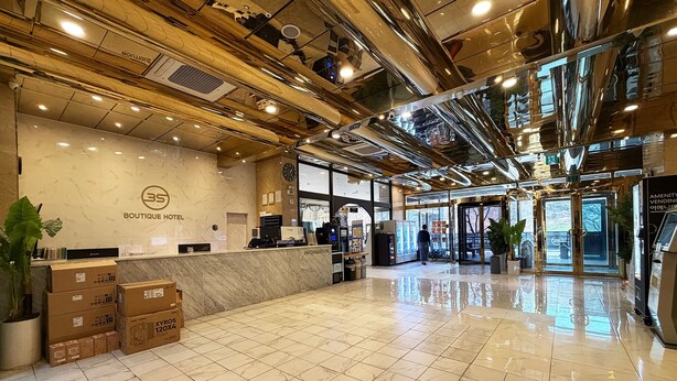 Uma área de recepção de hotel com piso de mármore, balcão de atendimento, um relógio e uma máquina de vendas automática.